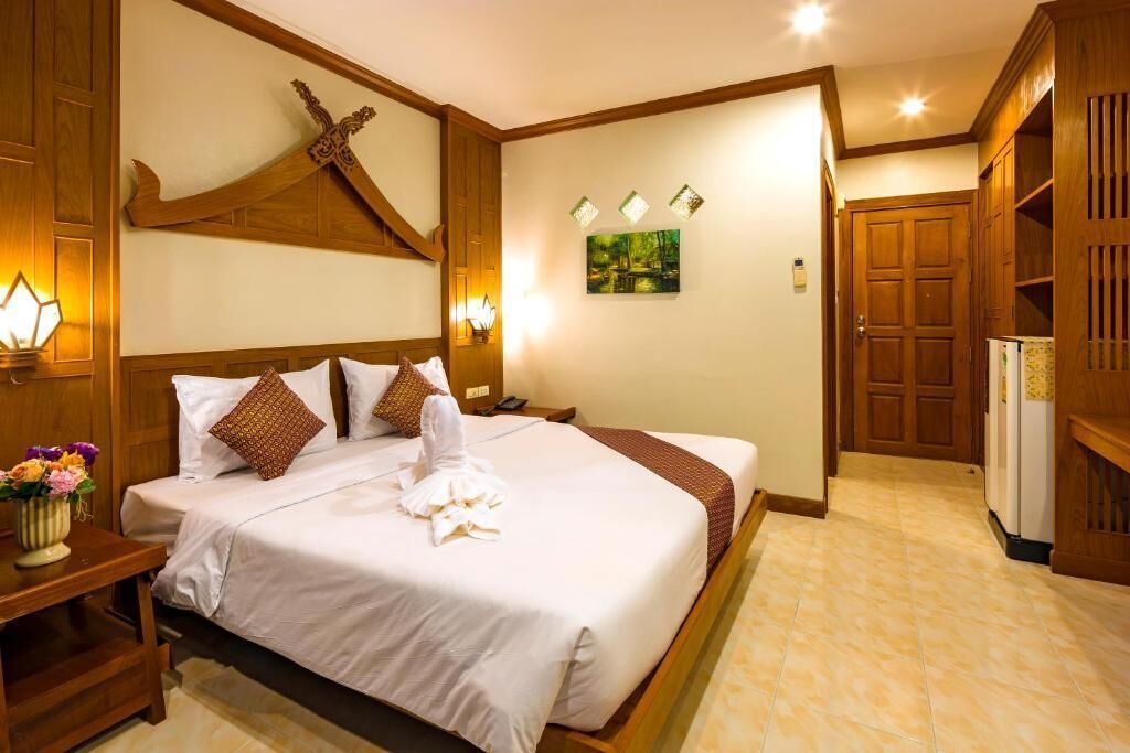 A hotel room with a large bed, wooden headboard, bedside lamps, a painting on the wall, and a wardrobe.