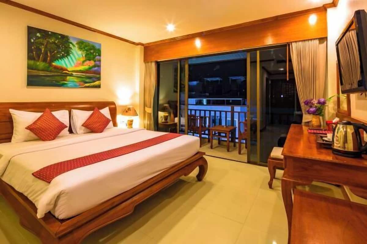 A hotel room with a large bed, a desk, a chair, a TV, and a balcony with a view of the night sky.