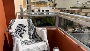 A balcony with a white table and a chair, a glass of wine, and a view of the cityscape.