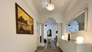 A hallway with patterned flooring, a painting on the left, and a mirror on the right.