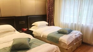 Une chambre d’hôtel avec deux lits, chacun étant équipé d’un oreiller et d’une couverture. Il y a une table de chevet avec une lampe et un objet rouge dessus. La chambre a un plancher en bois et une fenêtre avec des rideaux.