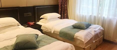 Two single beds with headboards, a bedside table with a lamp, and a window with sheer curtains.