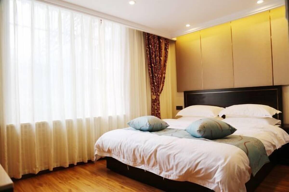 A bedroom with a large bed, a headboard, and a window with curtains.