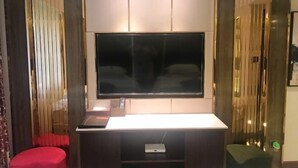 Un salon moderne doté d’un grand téléviseur à écran plat fixé au mur, d’une petite table sur laquelle repose une télécommande et d’un pouf rouge.