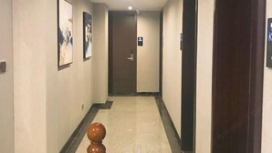 Un couloir d’hôtel avec des œuvres d’art encadrées accrochées aux murs, une porte en bois au fond et un petit objet décoratif posé sur le sol.