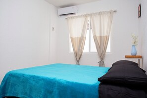 A room with a bed, a window with curtains, a wall-mounted air conditioner, and a small table with a vase. - Relaxing Cancun Pools Soccer & BBQ Area (Cancun)