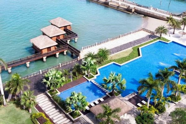 A resort with an infinity pool, overwater bungalows, and a palm tree-lined walkway.