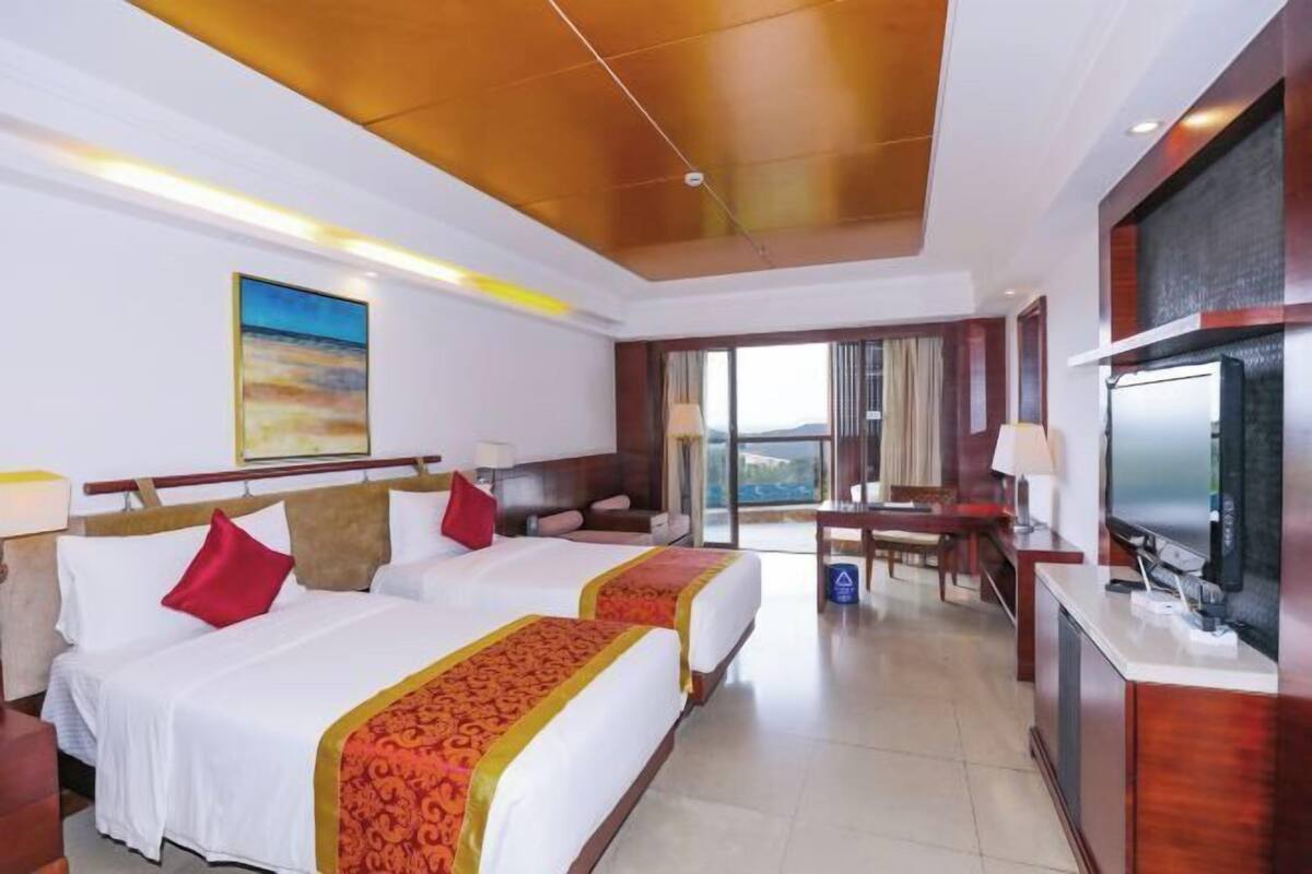 A hotel room with two beds, a television, a desk, and a view of the outdoors.