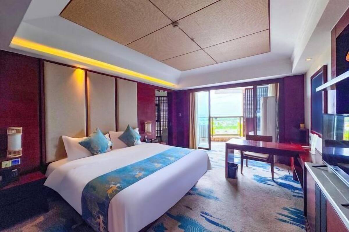 A hotel room with a large bed, a desk, a television, and a balcony with a view.