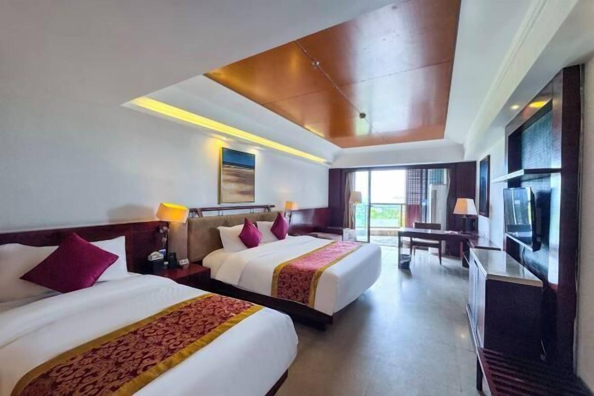 A hotel room with two beds, a TV, a desk, and a balcony.