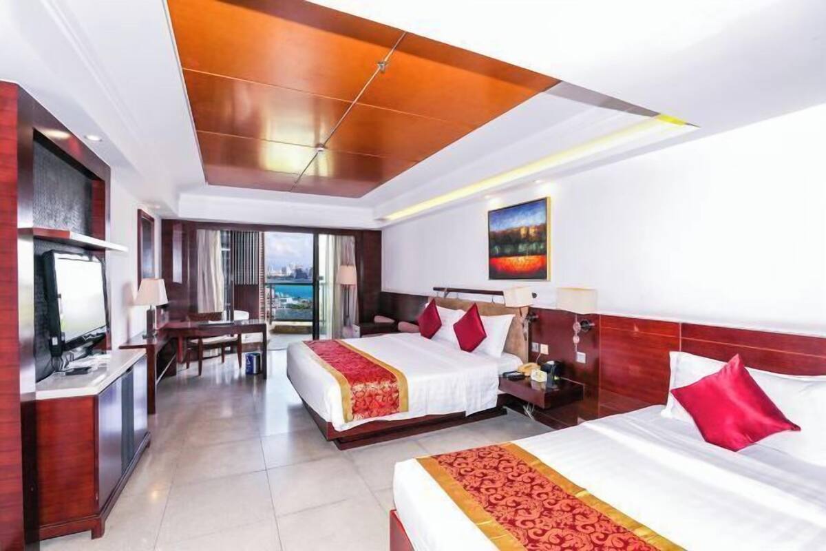 A hotel room with two beds, a desk, a television, and a view of the city.