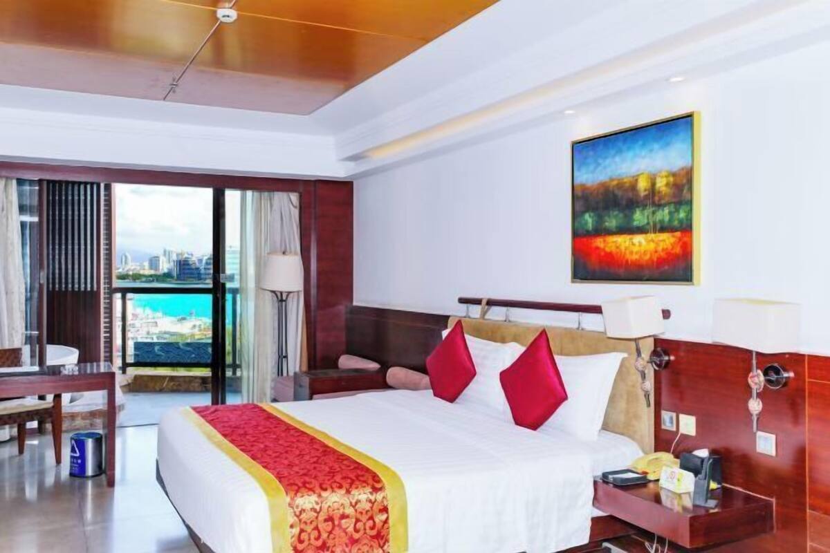 A hotel room with a bed, bedside table, lamp, and a painting on the wall.
