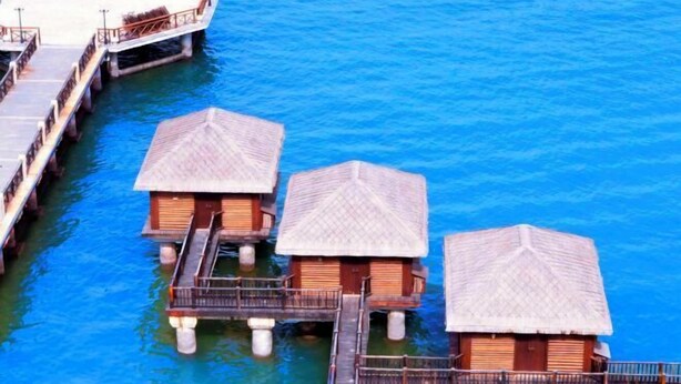 Des bungalows sur pilotis, dotés de structures en bois et de toits de chaume, reliés par des passerelles au-dessus d’une eau d’un bleu cristallin.