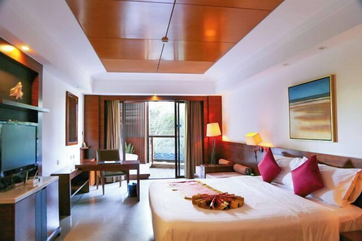 A hotel room with a bed, bedside table, lamp, and a view through a glass door.