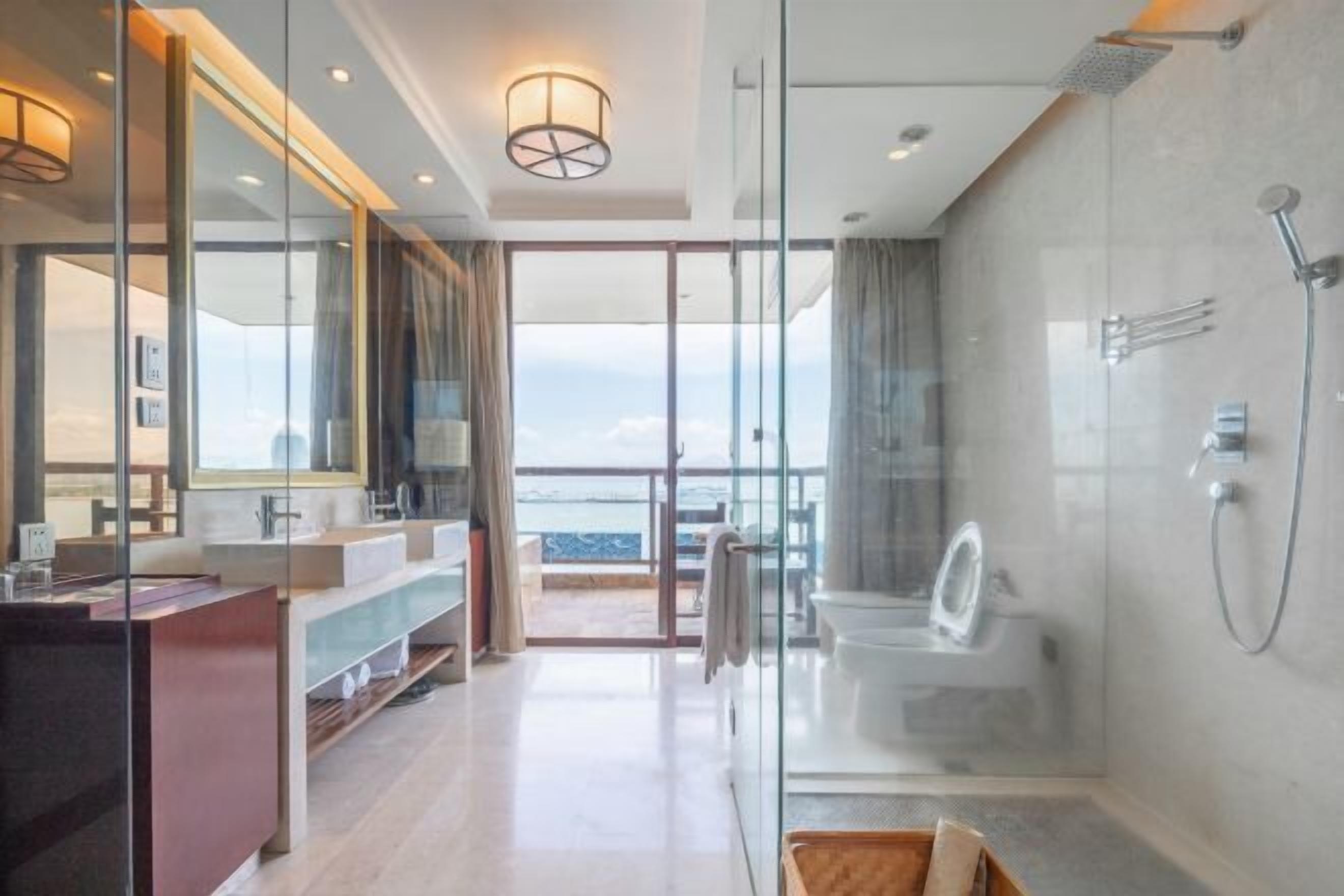 A modern bathroom with a glass shower enclosure, a vanity with a mirror, and a view of the ocean.
