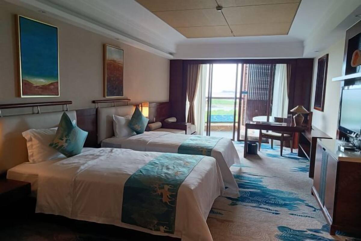 A hotel room with two beds, a desk, a chair, and a television.