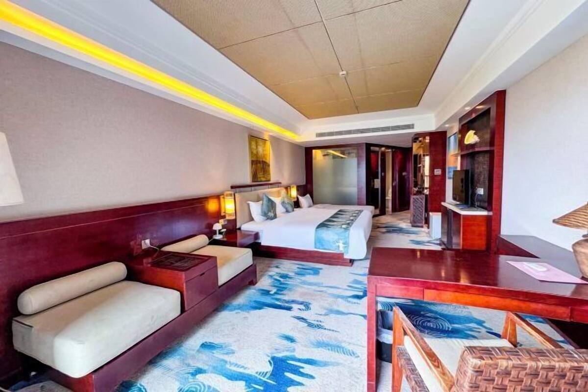 A hotel room with a large bed, a sofa, a desk, and a TV.