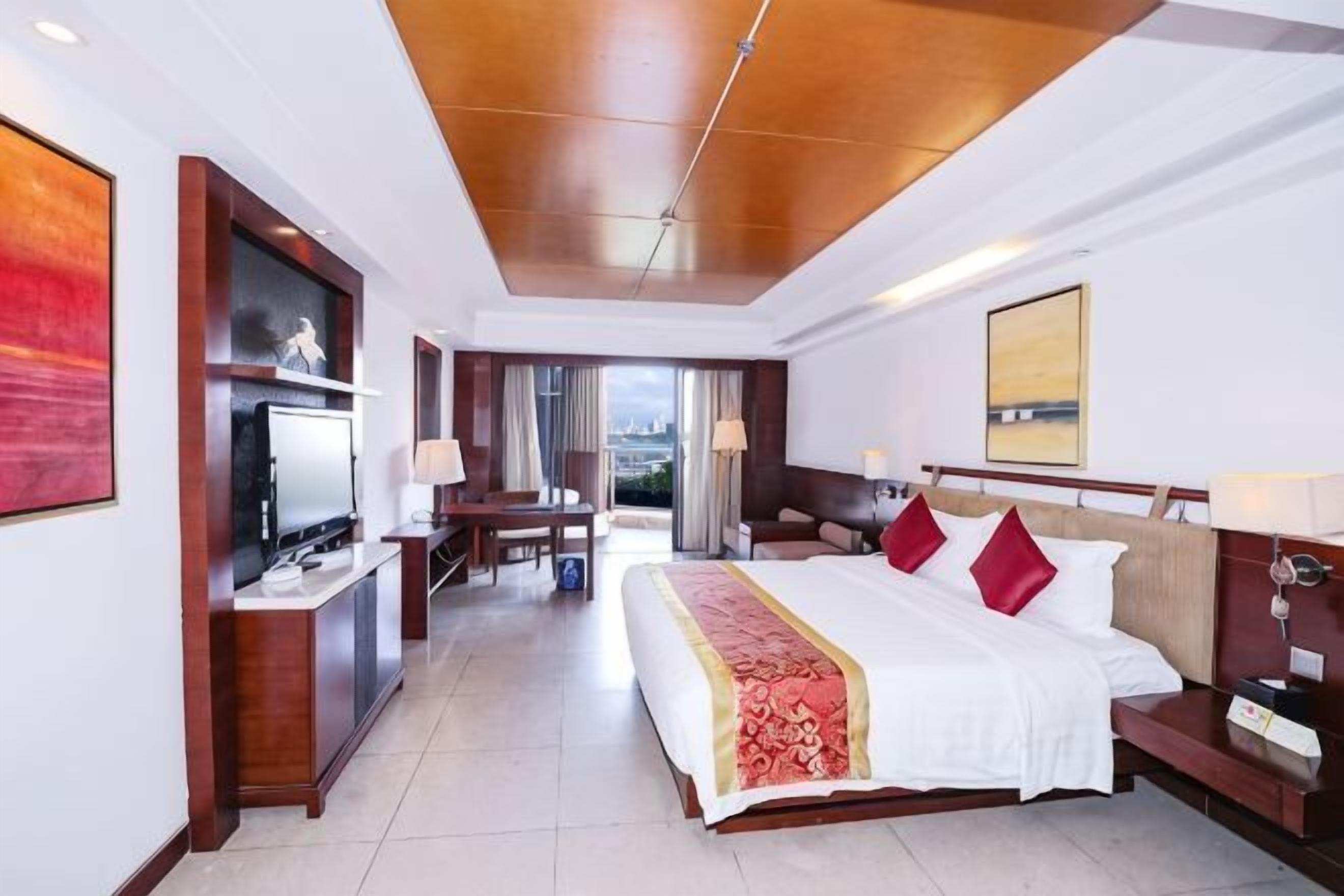 A hotel room with a large bed, a desk, a TV, and a view of the city.
