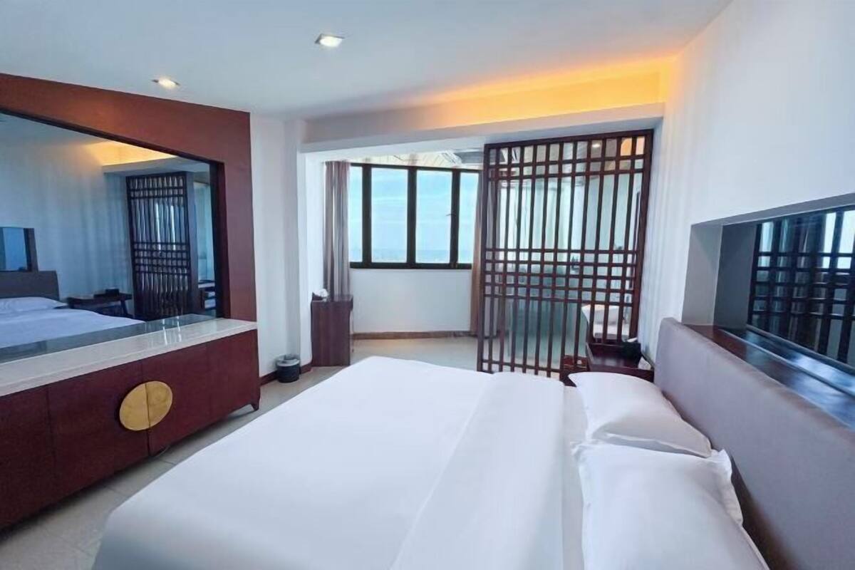 A hotel room with a large bed, a TV, a mirror, a window, and a balcony.