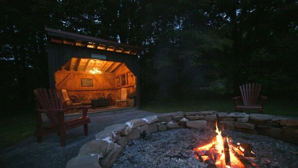 A cozy outdoor seating area with a fire pit, wooden chairs, and a stone fire ring. - Luxury Private Farmhouse Estate Near Salmon River (Altmar)
