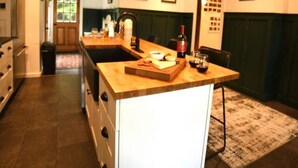 A modern kitchen with a wooden island, pendant lights, and a view into the dining area. - Luxury Private Farmhouse Estate Near Salmon River (Altmar)