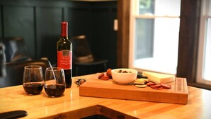 A wooden table with a bottle of wine, glasses, a bowl of nuts, and a block of cheese. - Luxury Private Farmhouse Estate Near Salmon River (Altmar)