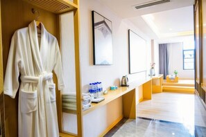 A hotel bathroom with a robe hanging, a towel rack, a mirror, and a shelf with toiletries. - Jianlang Holiday Hot Spring Hotel (Shilin)