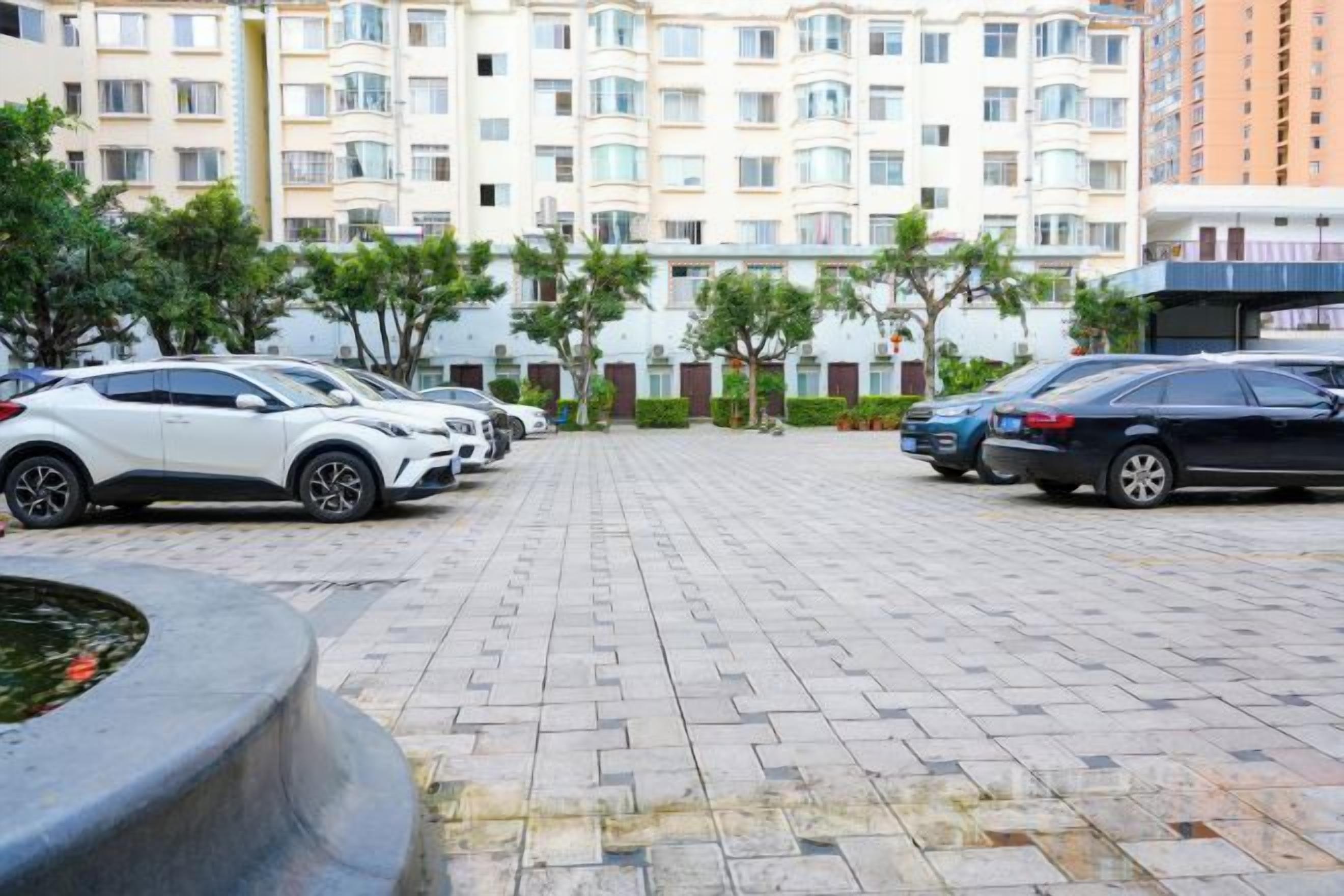 A parking area with cars, a paved walkway, and a building with multiple floors in the background.