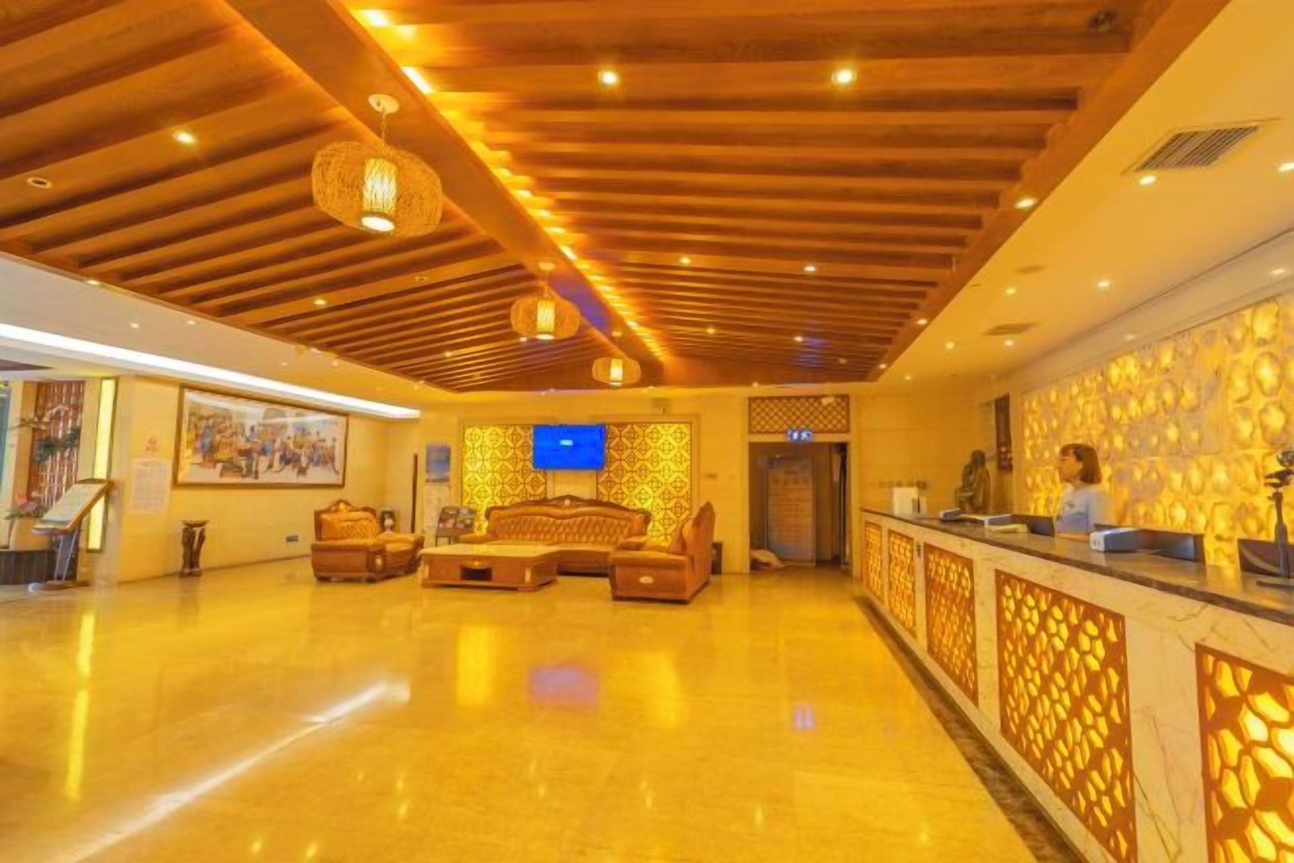 A hotel lobby with a reception desk, seating area, and a television screen.