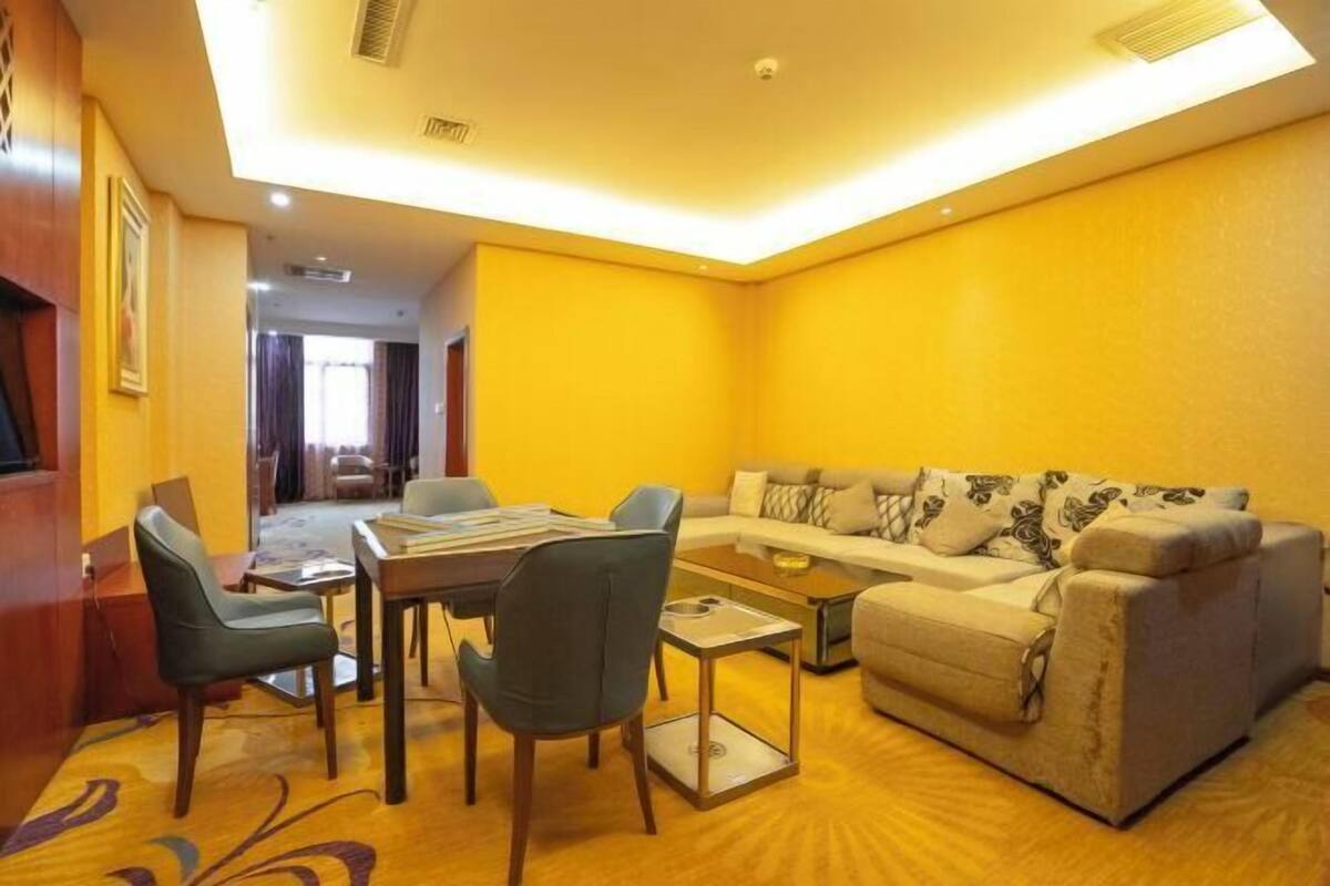 A hotel room with a yellow wall, a sofa, a coffee table, and a dining area with chairs and a table.