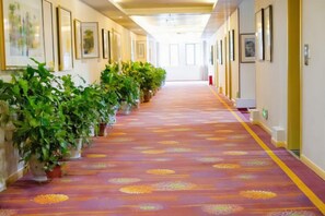 A hotel corridor with potted plants, framed pictures on the walls, and a patterned carpet. - Jianlang Holiday Hot Spring Hotel (Shilin)
