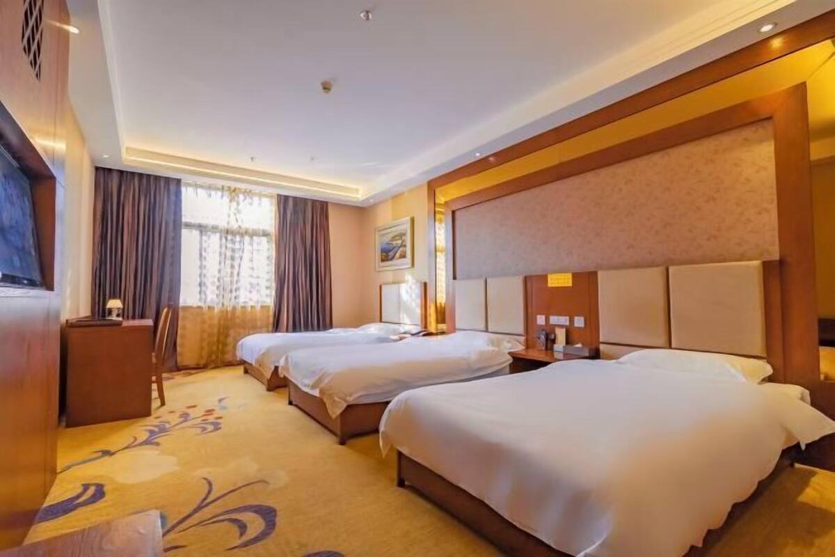 A hotel room with two beds, a desk, and a large window with curtains.
