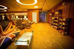 A hotel lobby with a patterned carpet, seating area with sofas and chairs, a reception desk, and a bookshelf. - Jianlang Holiday Hot Spring Hotel (Shilin)