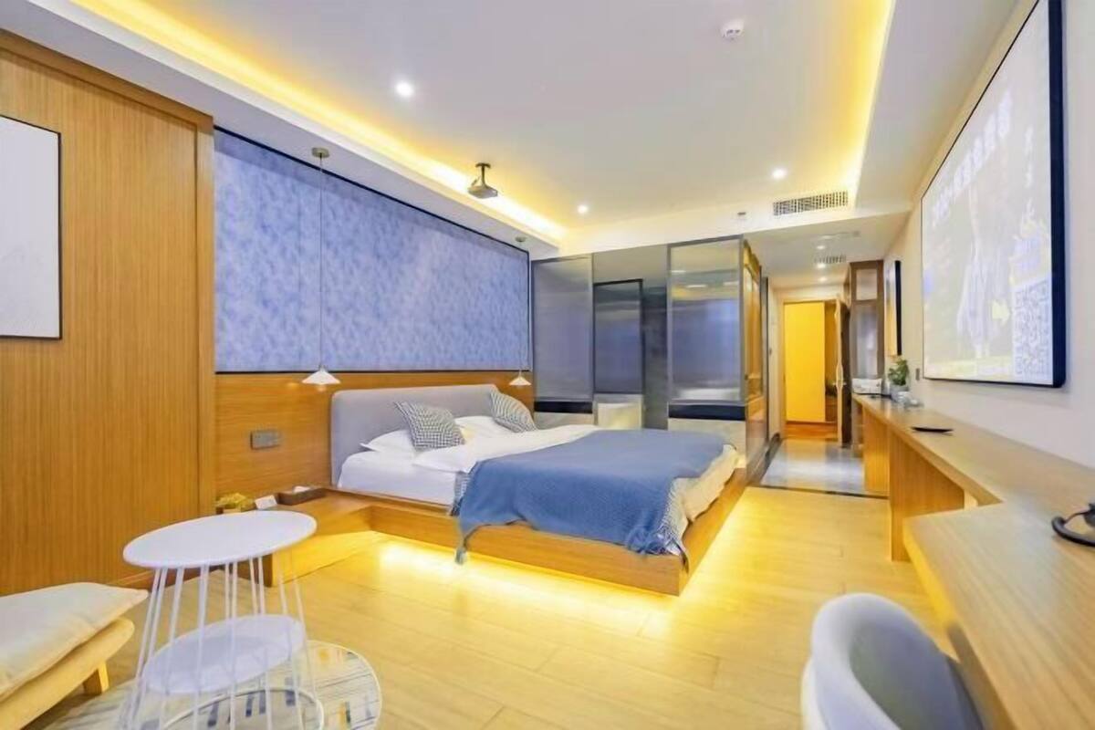A modern hotel room with a bed, bedside tables, a seating area, and a large window.