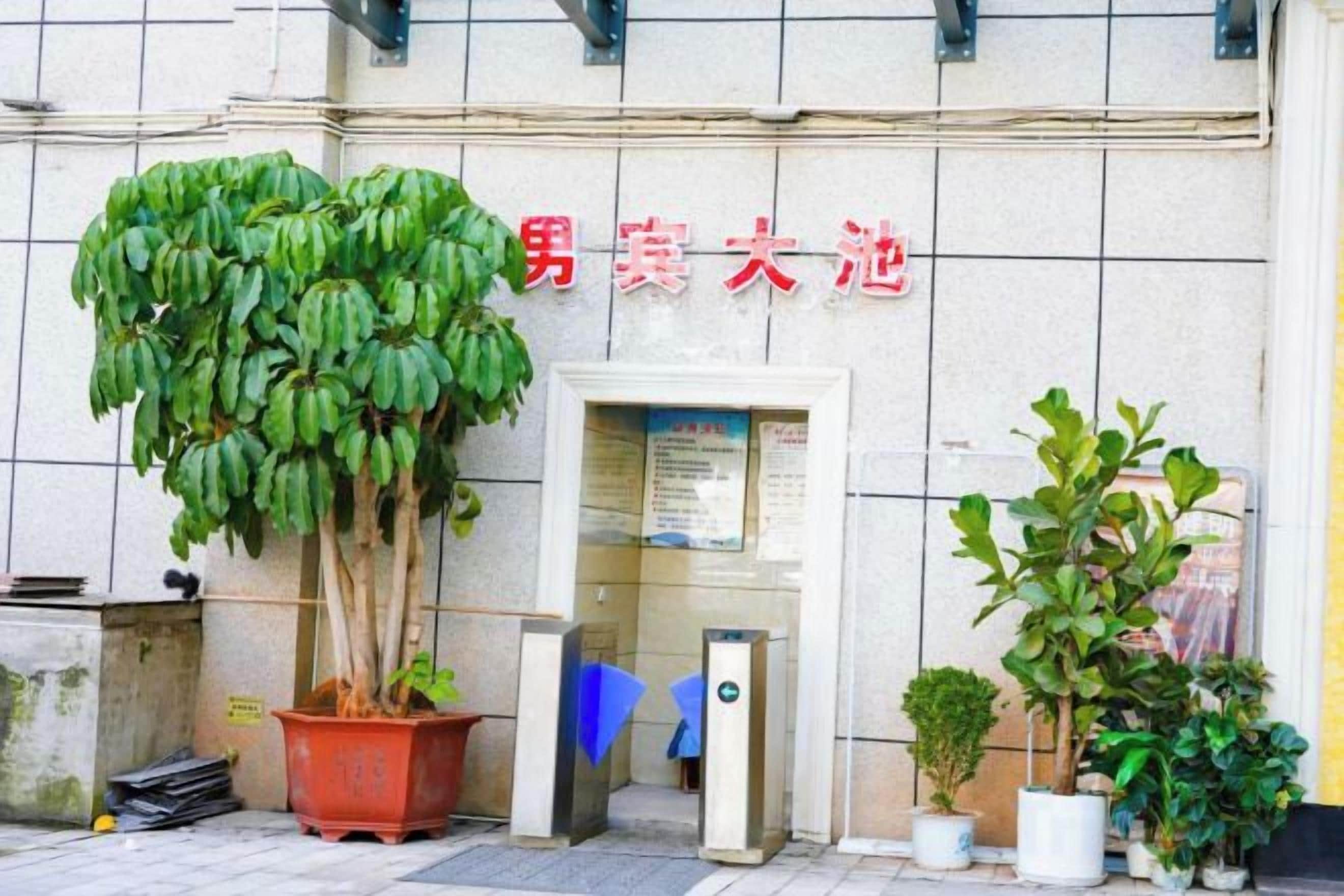 Una entrada de edificio con un letrero en caracteres rojos, una planta en maceta y una puerta.