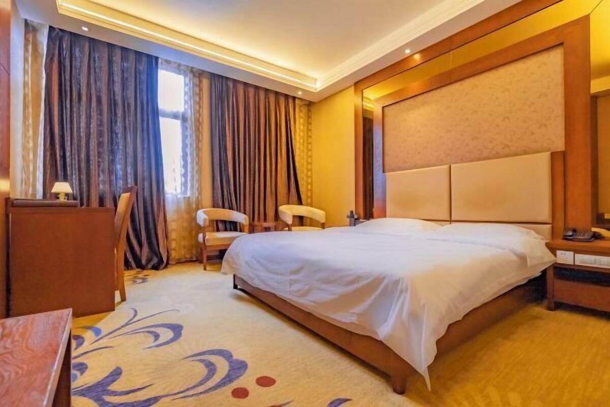 A hotel room with a large bed, a desk, a chair, and a window with curtains.