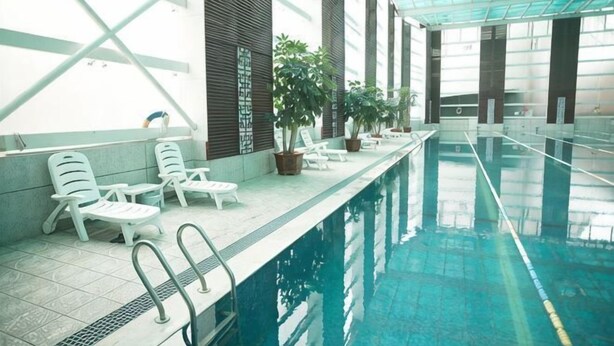 An indoor swimming pool with lounge chairs, potted plants, and a tiled floor. - Jianlang Holiday Hot Spring Hotel (Shilin)