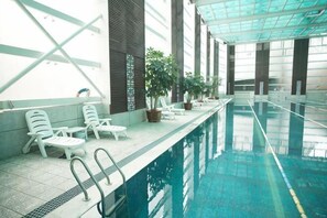 Una piscina interior con sillones de descanso, plantas en macetas y suelo de baldosas.