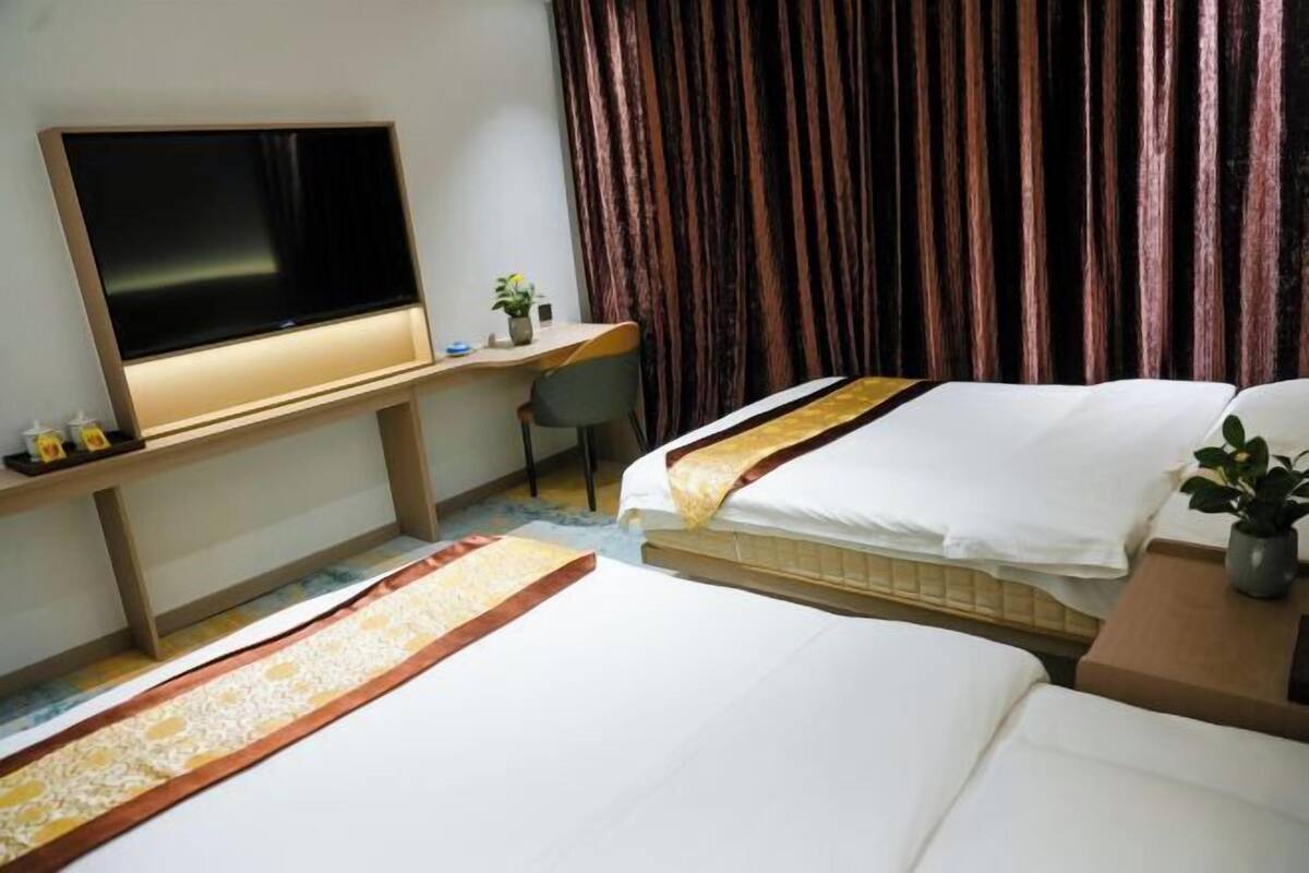 A hotel room with a bed, a desk with a TV, and a curtain.