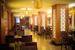 Un restaurant avec des tables et des chaises, des piliers en bois ornés de motifs géométriques et des luminaires suspendus.