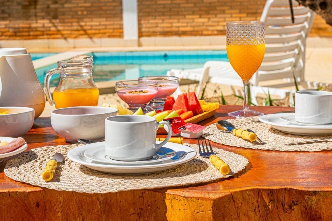 A breakfast setup with a wooden table, white cups, plates, and a fruit platter.