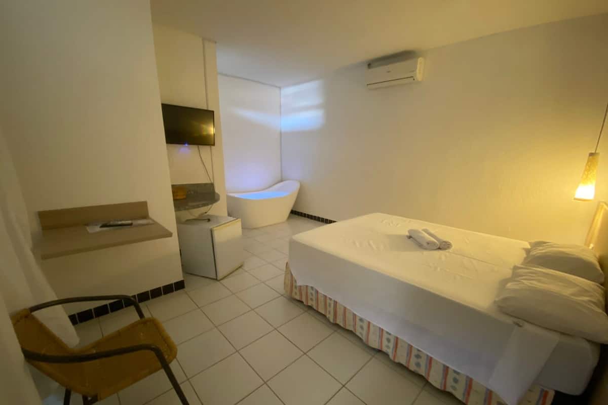 A hotel room with a bed, a small desk, a chair, a bathtub, and a TV.