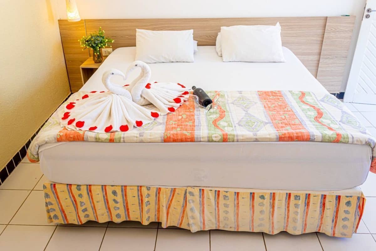 A neatly made bed with a colorful blanket, a swan-shaped towel arrangement, and a small table with a plant.