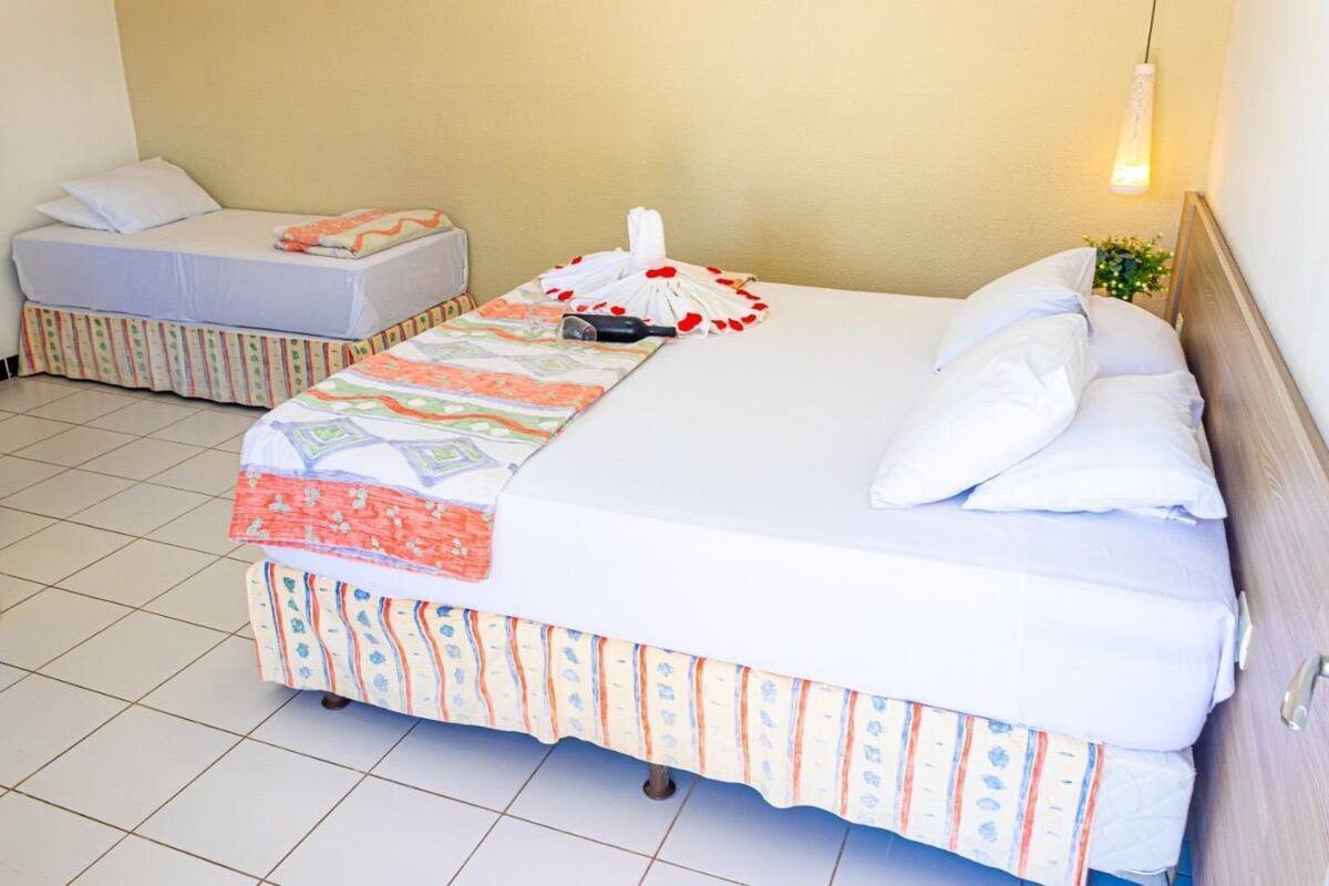 A double bed with a patterned bedspread and pillows, a bedside table with a lamp, and a small plant on the nightstand.