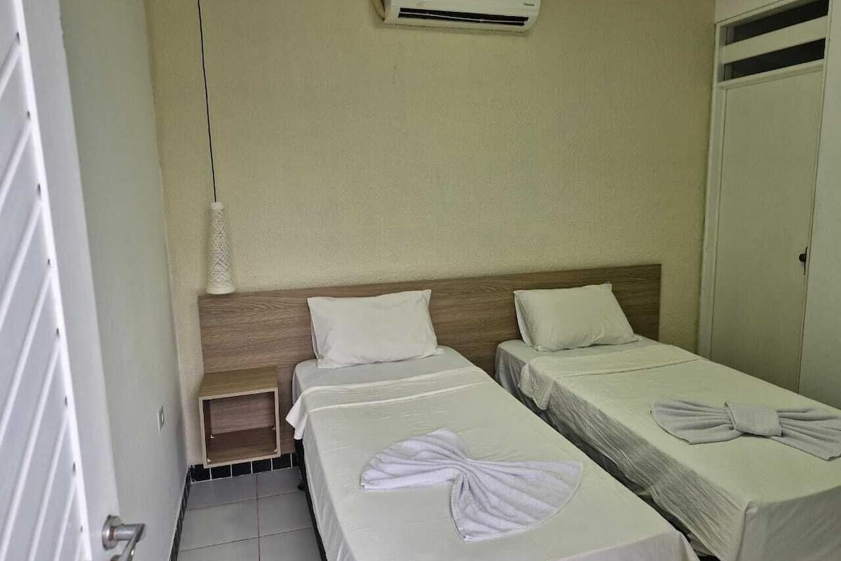 A hotel room with two single beds, a wooden headboard, a nightstand, and a wall-mounted air conditioner.
