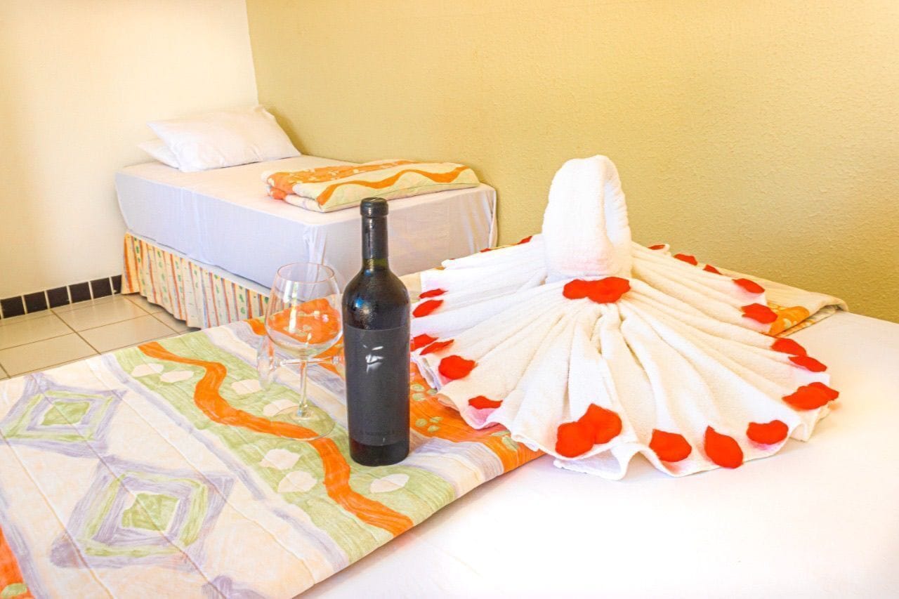 A hotel room with a bed, a bottle of wine, a glass, and a towel arranged in a fan shape.