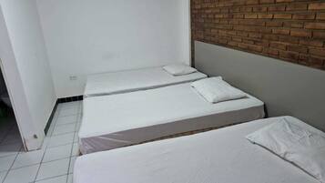 A small, clean room with two single beds, white bedding, and a brick accent wall.