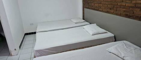 A small, clean room with two single beds, white bedding, and a brick accent wall.