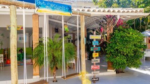 Un espacio al aire libre techado con un conjunto de columpios, palmeras y un cartel con indicaciones hacia diferentes instalaciones.