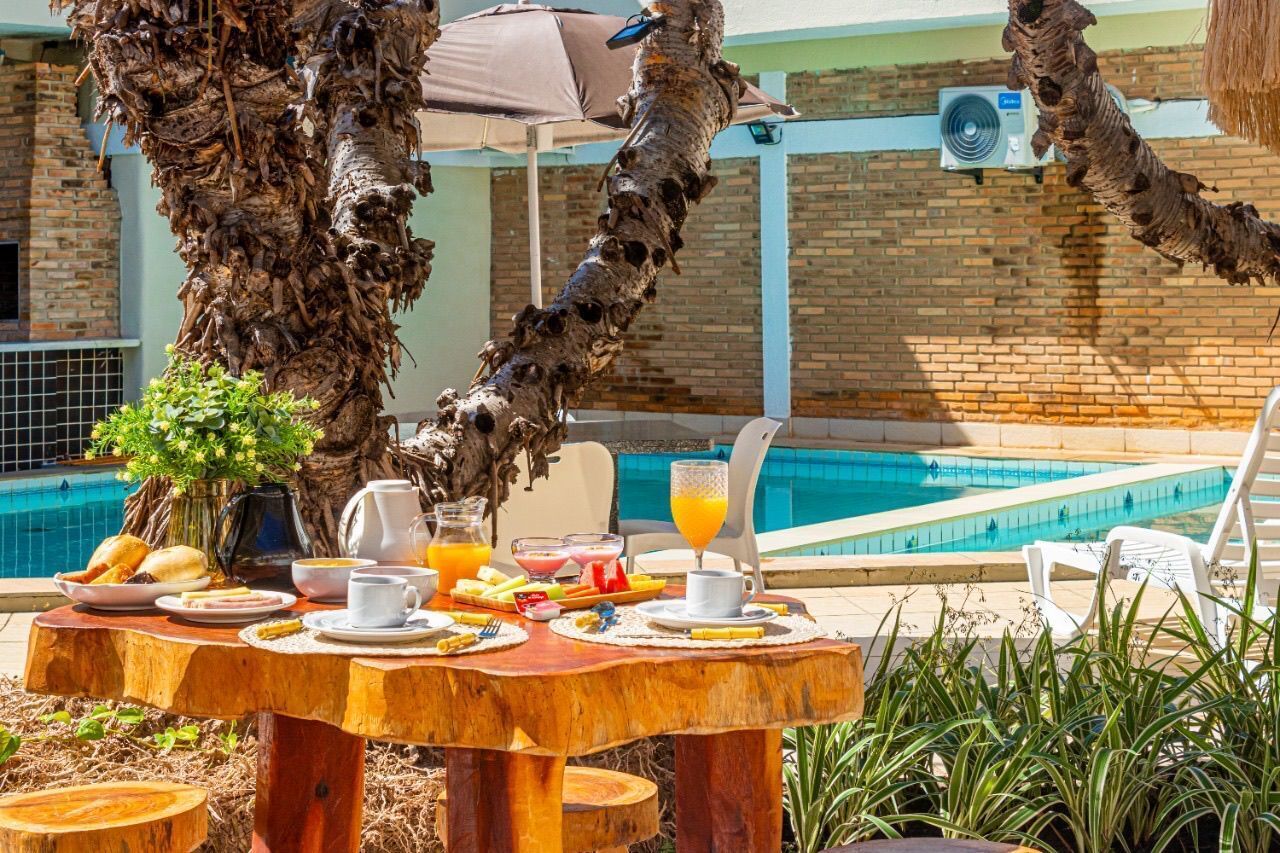 Ein Holztisch ist reichhaltig mit Frühstücksartikeln gedeckt, im Hintergrund ist ein Pool und eine Ziegelwand zu sehen.